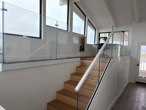 Continuous frameless glass wraps a loft edge and follows an oak stair below black-framed clerestory windows.
