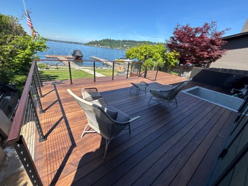 Wood-capped black cable railing lines a hardwood deck with lounge chairs overlooking a lake and docks.