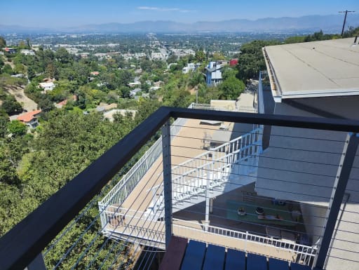 A dark-capped cable railing corner frames a sweeping view over wooded hills and a distant valley.