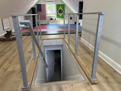 Silver cable railing with an angled stair section surrounds a stair opening in a finished attic room.