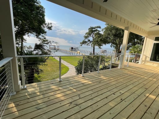 White cable railing lines a wide covered porch looking out over a lawn and waterfront docks.