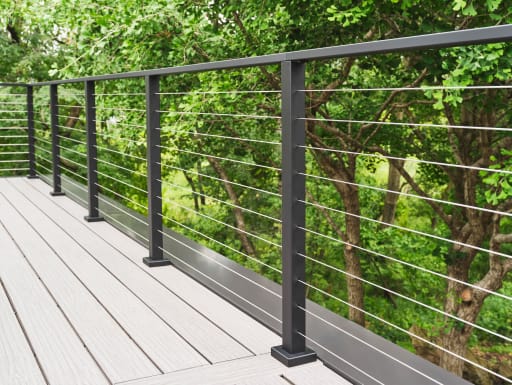 A long run of black Express cable railing on a pale composite deck against lush green foliage.
