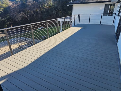 Side-mount Express cable railing surrounds a wide composite deck on a white home.