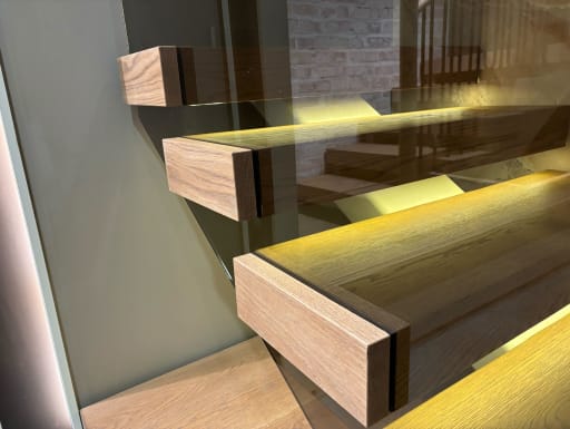 Close view of thick oak floating treads glowing with warm LED light behind a frameless glass guard.
