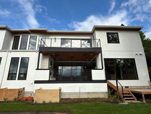 Rear of a white modern home with jet black cable railing on the upper balcony, lower terrace and deck stair.