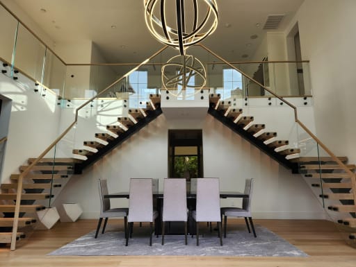 Symmetrical pair of black mono stringer floating stairs with oak treads and frameless glass rising to a loft above a dining room.