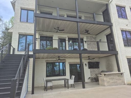 Dark cable railing on two stacked covered decks and a long exterior stair on a white brick home.