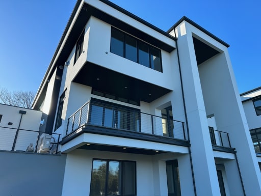 Dark cable railing on cantilevered balconies of a white modern home against a blue sky.