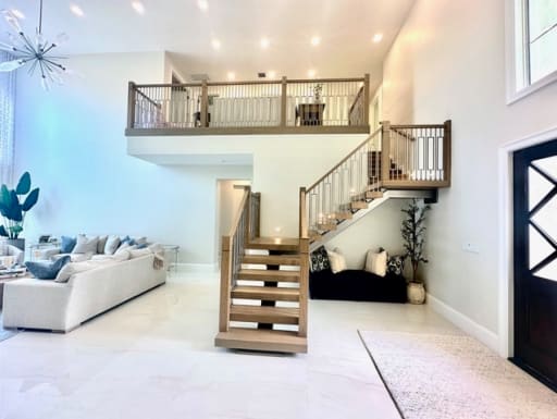 Oak floating treads with a wood and metal railing lead up to a matching loft balustrade above a white living area.