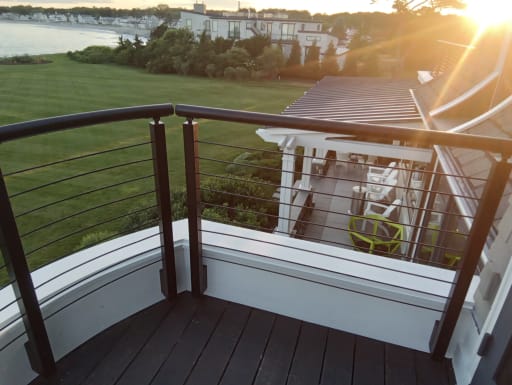 Bronze posts and rod infill with round handrail on a curved deck wall with sun flare over the coast.