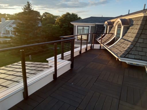 Rod railing with round handrail lining a rooftop deck beside slate-shingled dormers.