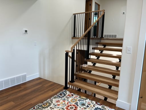 Open hickory treads on black stringers with a black baluster railing and hickory handrail in a bright entry.