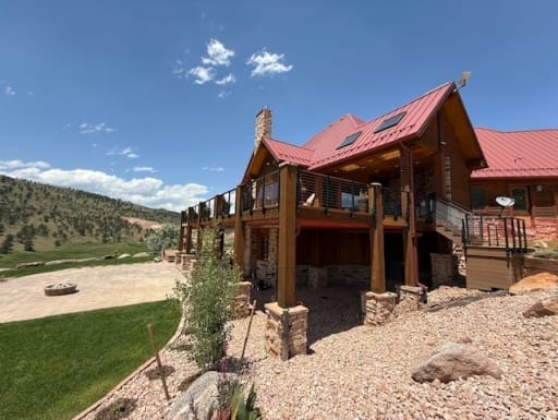 Wide view of a red-roofed lodge with a wraparound deck finished in black cable railing.