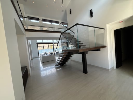 Dark floating treads on a black mono stringer with frameless glass railing rise to a glass-railed loft in a white double-height room.