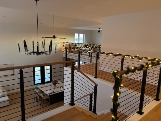 Black cable railings trimmed with holiday garland surround a stair opening and loft overlooking a dining area.