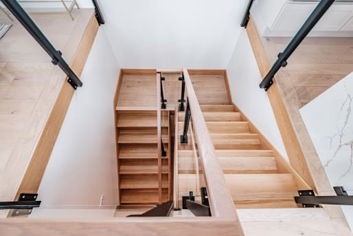 Looking down a white oak switchback stair lined with black-post glass railing and oak handrails.