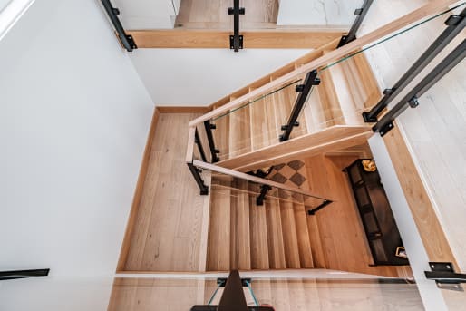 Top-down view of an oak stair turning at a landing with black side-mount glass posts and oak rails.