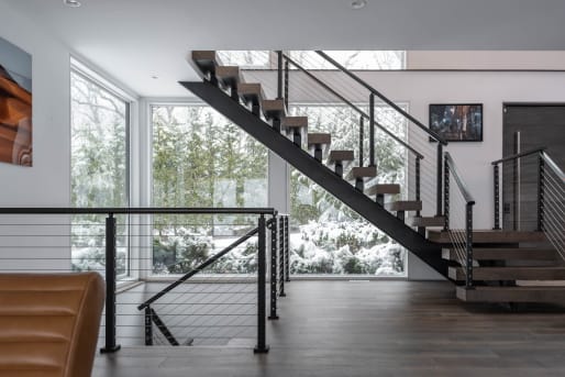 A black FLIGHT Mono with stained oak treads and cable railing rises past snow-covered windows.