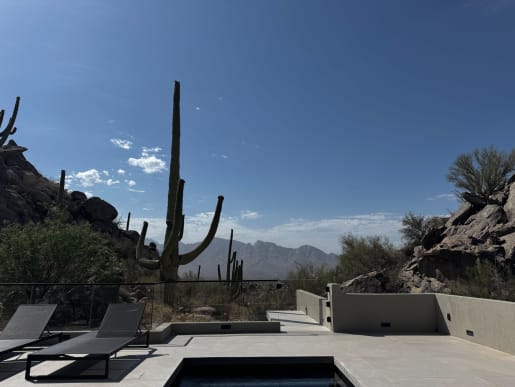 Frameless glass railing edges a desert pool terrace with saguaro cacti and mountains beyond.