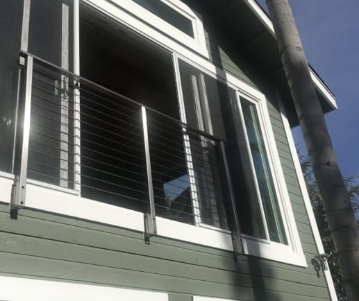Stainless cable railing guards a tall window balcony on a green-sided home.