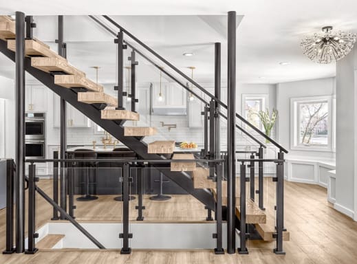 Black FLIGHT mono stringer with rustic oak treads and black post-to-post glass railing in front of a bright white kitchen.
