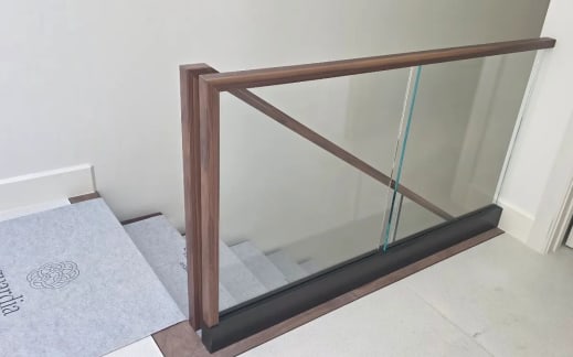 Frameless base rail glass with a walnut cap and squared walnut newel at the head of a stair
