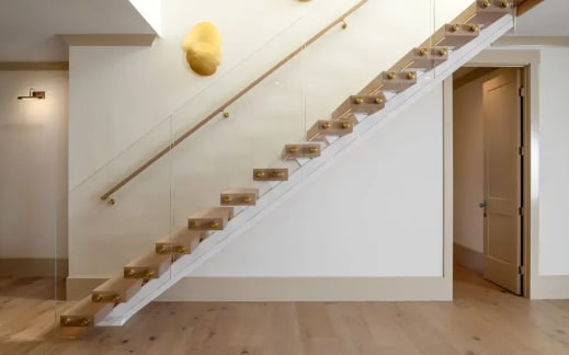 Oak treads on a white plaster stringer with glass held by brass standoff pins and a wood handrail.