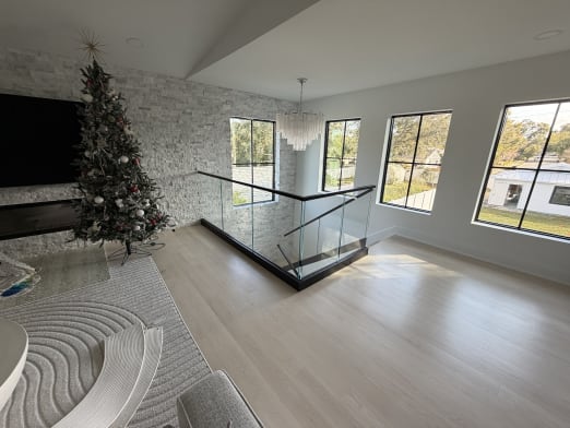 Frameless glass in a black base rail with a black cap guards a stair opening in a bright living room.