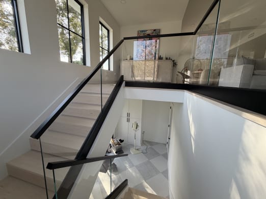 Frameless glass on a kneewall base rail with a black handrail runs along a white oak stair to a glass-railed loft.