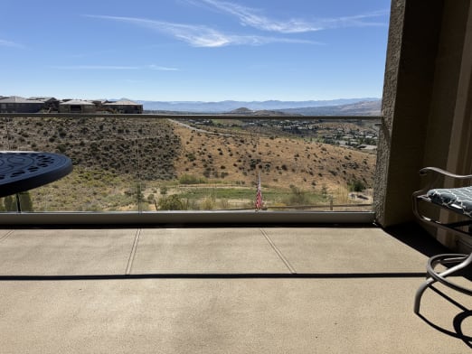 A glass railing with slim cap runs across a covered patio with a wide view of hills and valley.