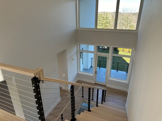 Black-post cable railing with oak handrail looks down a white oak stair to a window-filled entry.