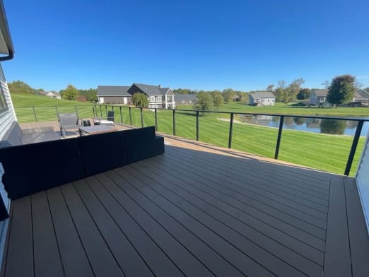 Black cable railing surrounds a wide composite deck overlooking a pond and neighborhood lawns.