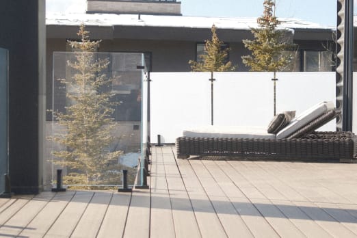 Clear and frosted glass panels on black spigots enclose a rooftop deck with a lounge chair.