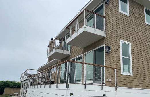 Side-mounted cable railing with wood top rail on balconies and a deck of a cedar-shingle home.