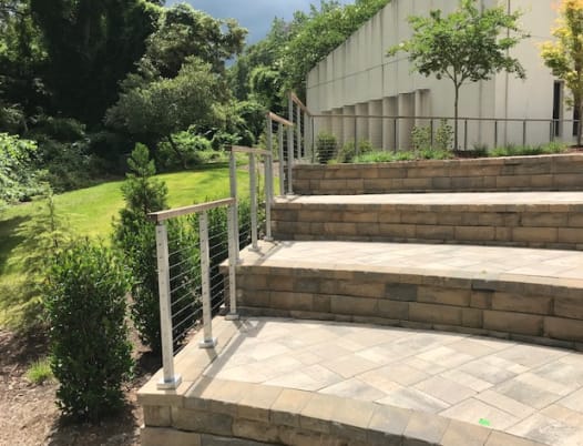 Stainless-post cable railing with a thermally modified wood top rail follows curved stone garden steps.