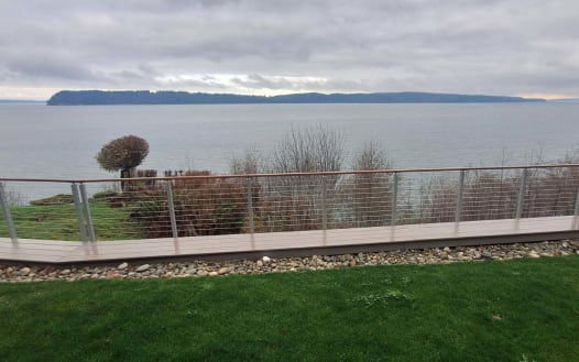 Polished stainless posts with cable infill line a curving IPE walkway along a lawn overlooking the water.
