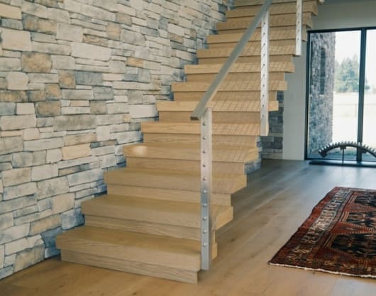 White oak stack stair with stainless cable posts rises along a stacked stone wall.