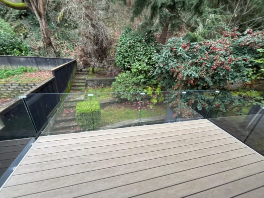Frameless glass railing on standoff pins edges a composite deck overlooking a lush terraced garden.