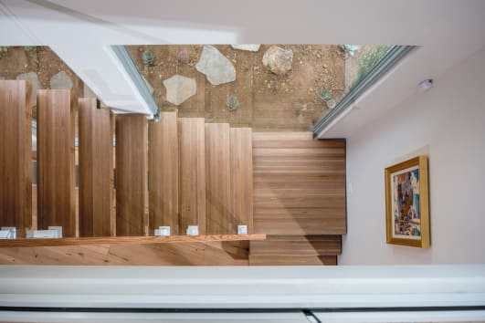 Looking down on wood treads and a landing edged with frameless glass on white talons.
