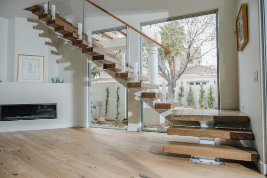 A white mono stringer stair with thick wood treads rises from stacked plinths beside frameless glass on white talons.