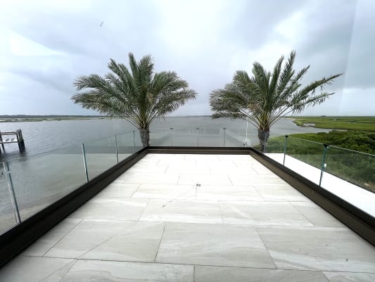 Base rail glass wraps a rooftop terrace with palms and a bay view