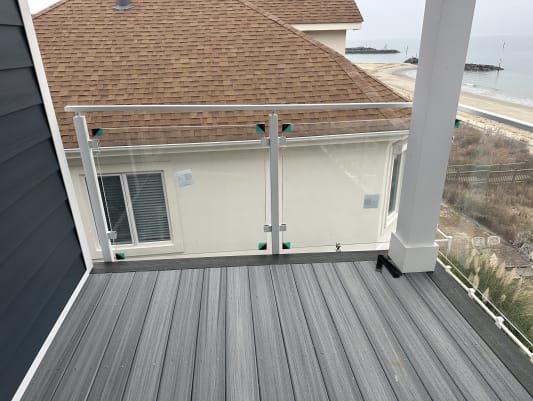 White post glass railing on a composite balcony overlooking a beach and breakwater