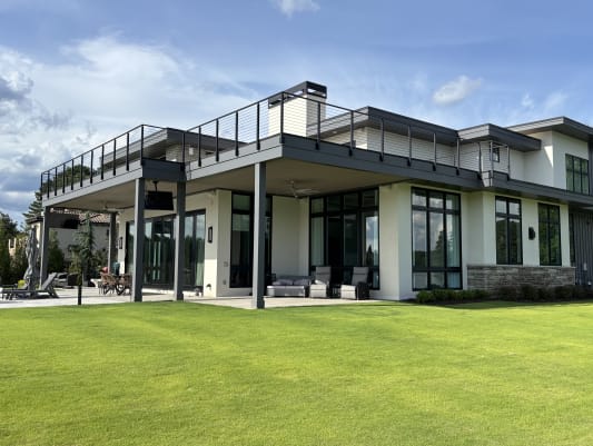 Side-mount Onyx rod railing lines the upper deck of a modern white lake house over a green lawn