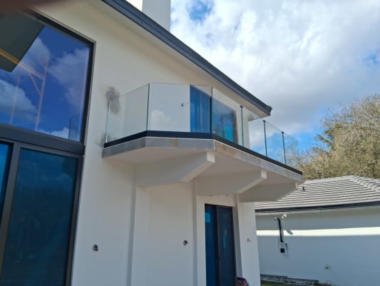 Frameless base rail glass balcony on a white stucco home under a blue sky