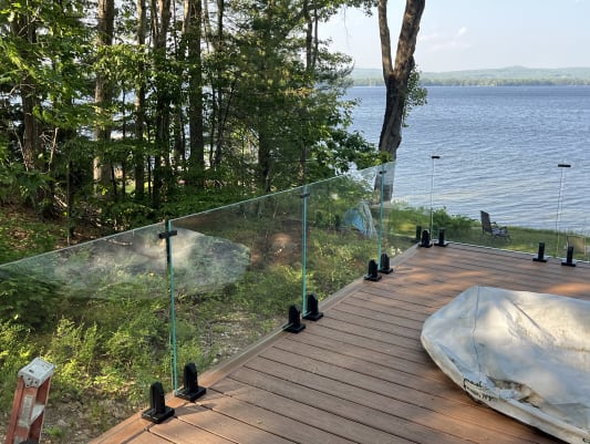 Frameless laminated glass on jet black surface talons edges a deck among pines above a lake