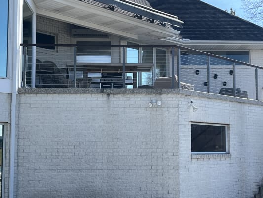 Gray-post cable railing with a dark top rail along a covered terrace on a white brick home