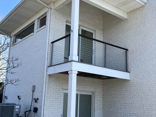 Small balcony with cable railing and wood cap above a patio door on a white brick home