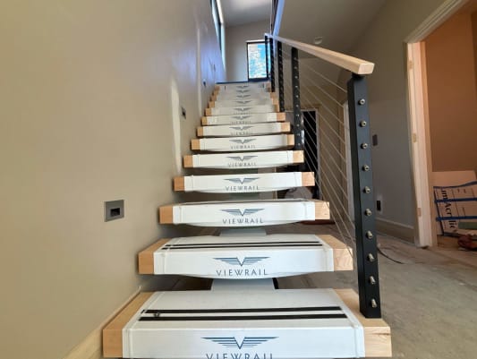 Floating stair in clean Viewrail tread covers with black cable railing and maple handrail