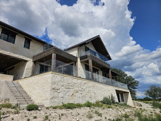 Frameless glass on talon spigots lines two terraces of a limestone hill-country home