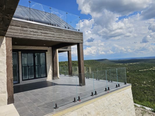 Frameless glass on black talon spigots edges a stone terrace overlooking rolling Texas hill country